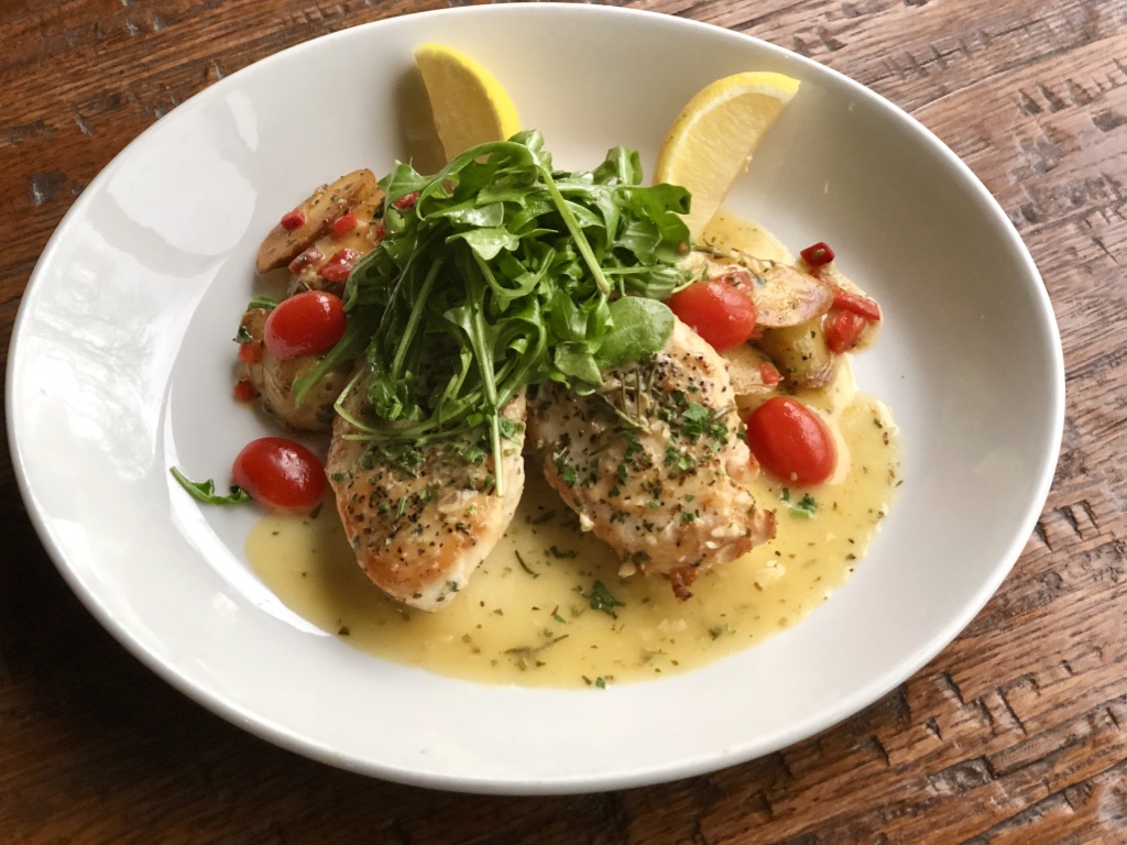 Grilled pork chops seasoned with herbs, served on a white plate with roasted vegetables