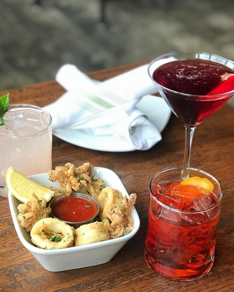 Two colorful cocktails served with a gourmet appetizer plate featuring fresh ingredients and vibrant presentation.